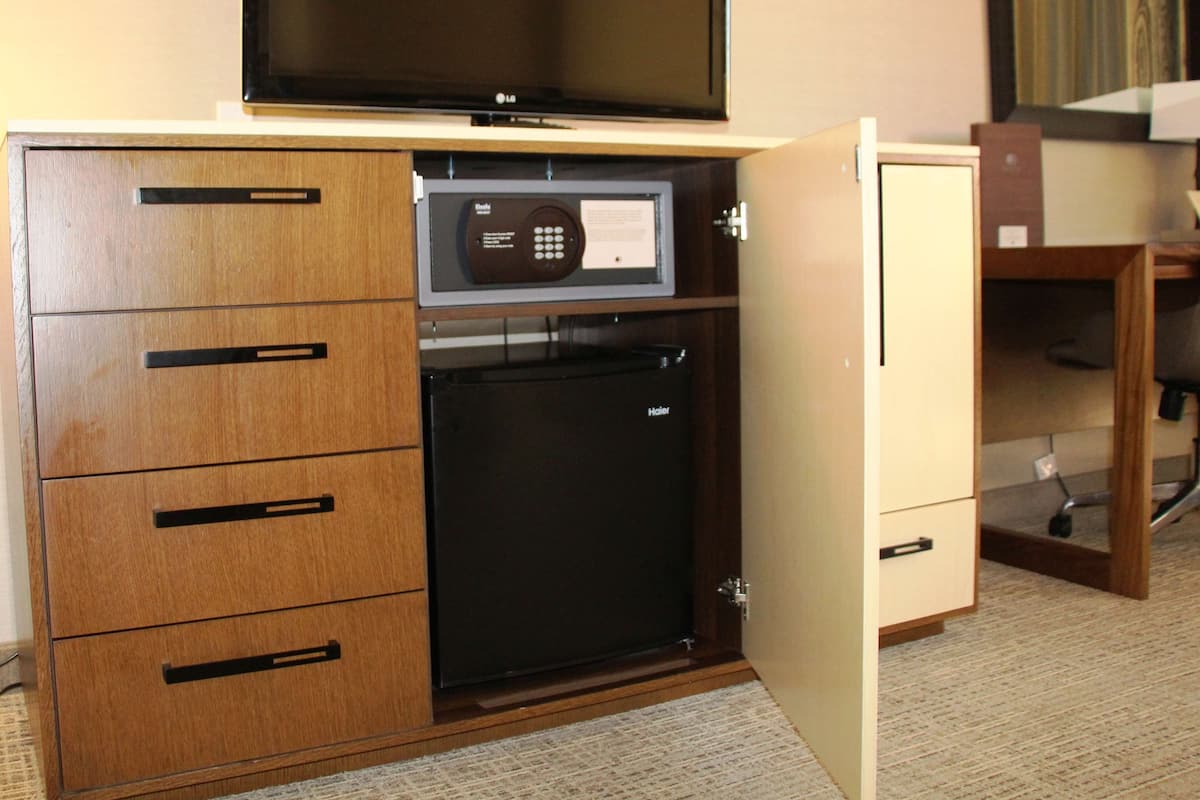 A hotel room with a minibar, a television, and a desk with a chair.