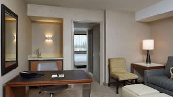 Quarto de hotel com secretária de madeira, uma cadeira, sofá, luminária e espelho.