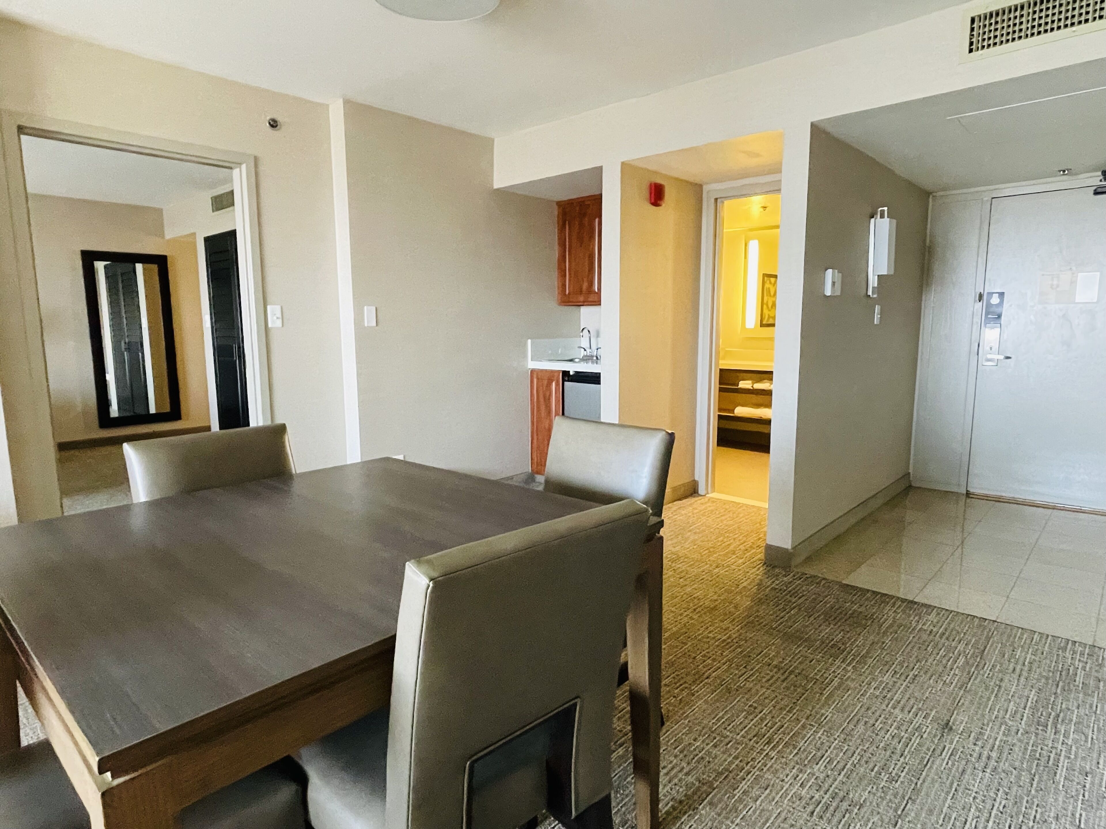 Un comedor con una mesa y sillas de madera, una cocina al fondo y una puerta que da a un armario.