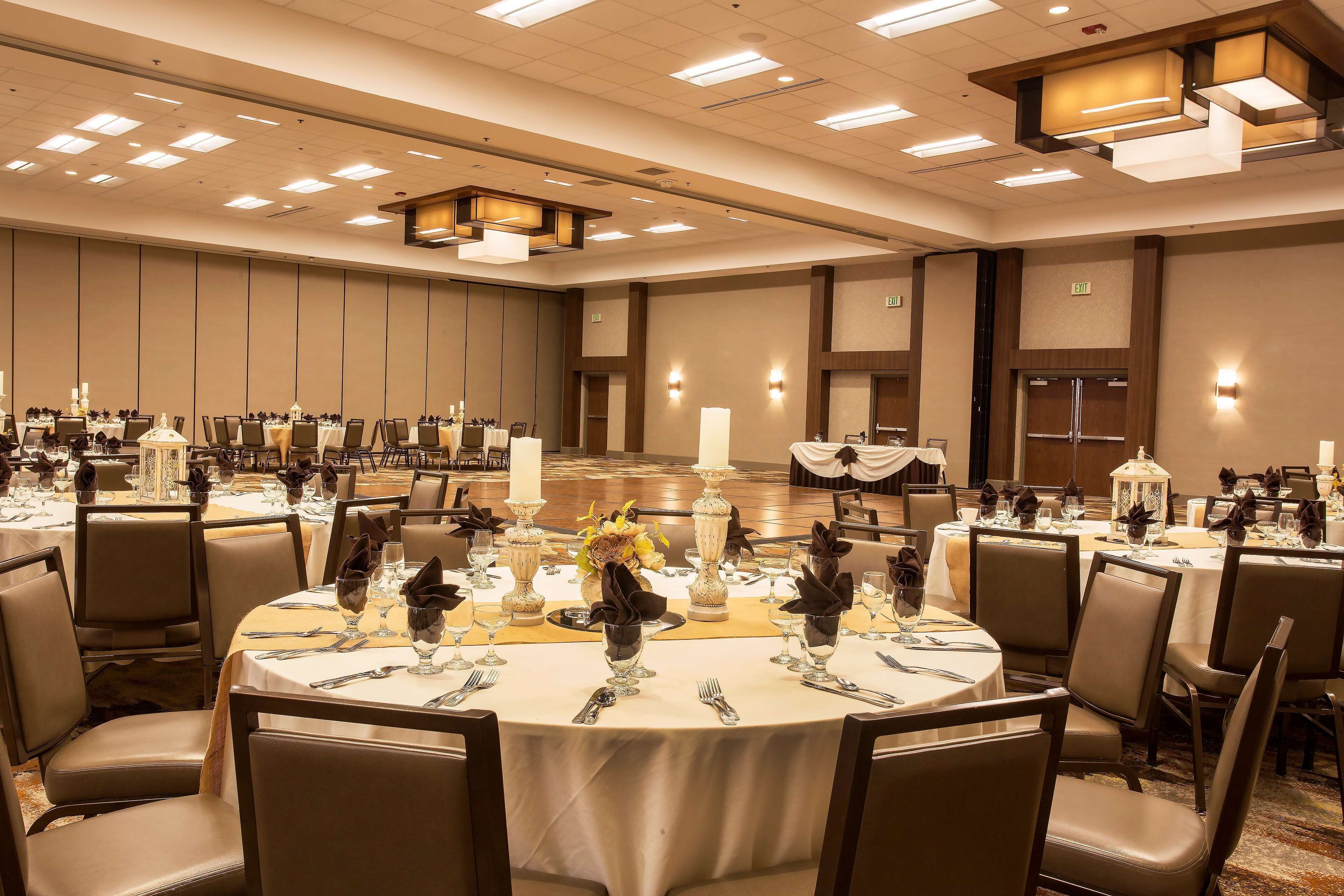 A banquet hall with round tables set for dining, featuring white tablecloths, dark napkins, and candle centerpieces.
