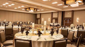 A banquet hall with round tables set for dining, featuring white tablecloths, dark napkins, and candle centerpieces.