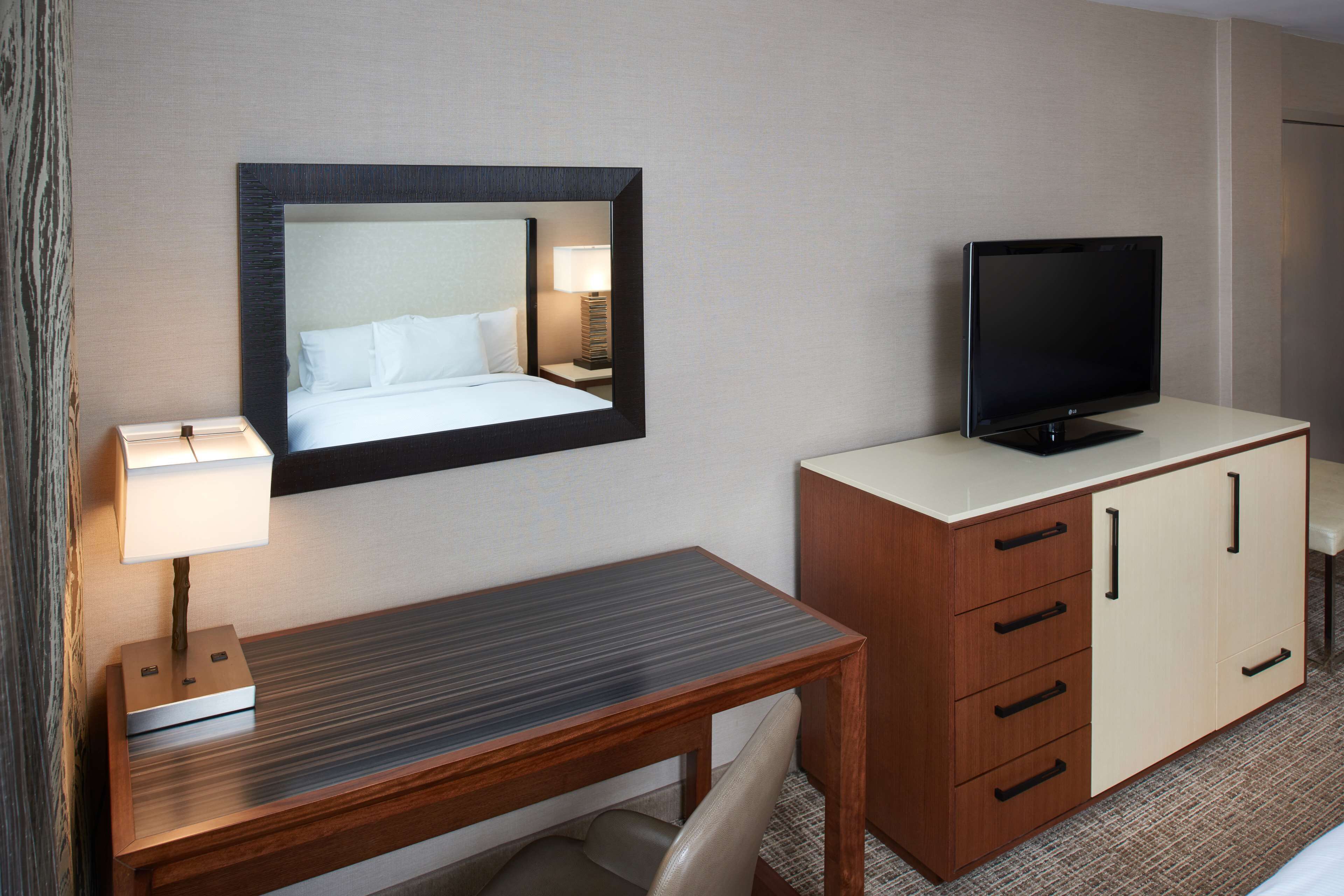 Una habitación de hotel con cama, escritorio con lámpara, televisor y armario.
