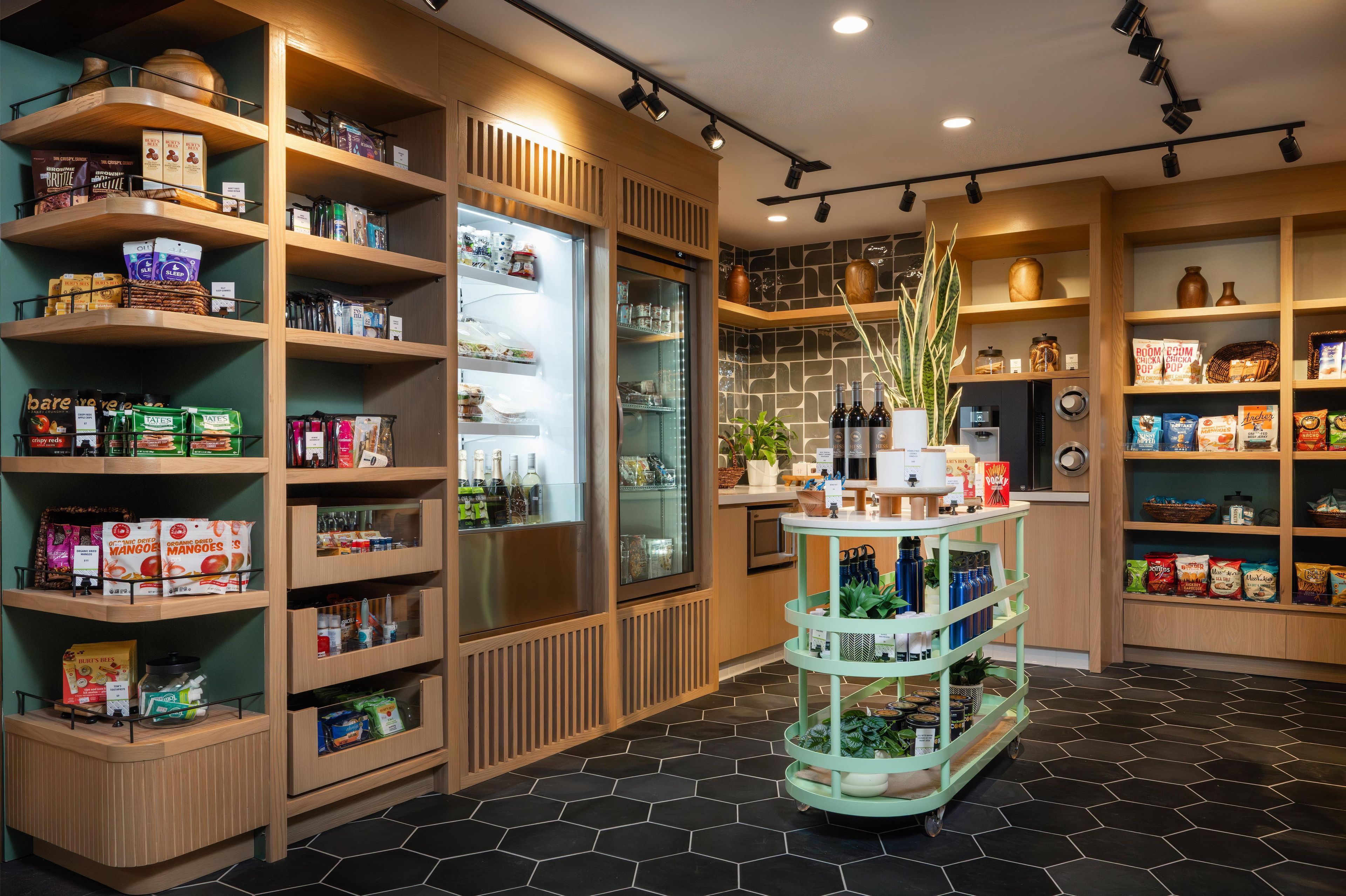Un magasin bien organisé, avec des étagères remplies de divers produits alimentaires et un présentoir central où sont exposées des bouteilles.