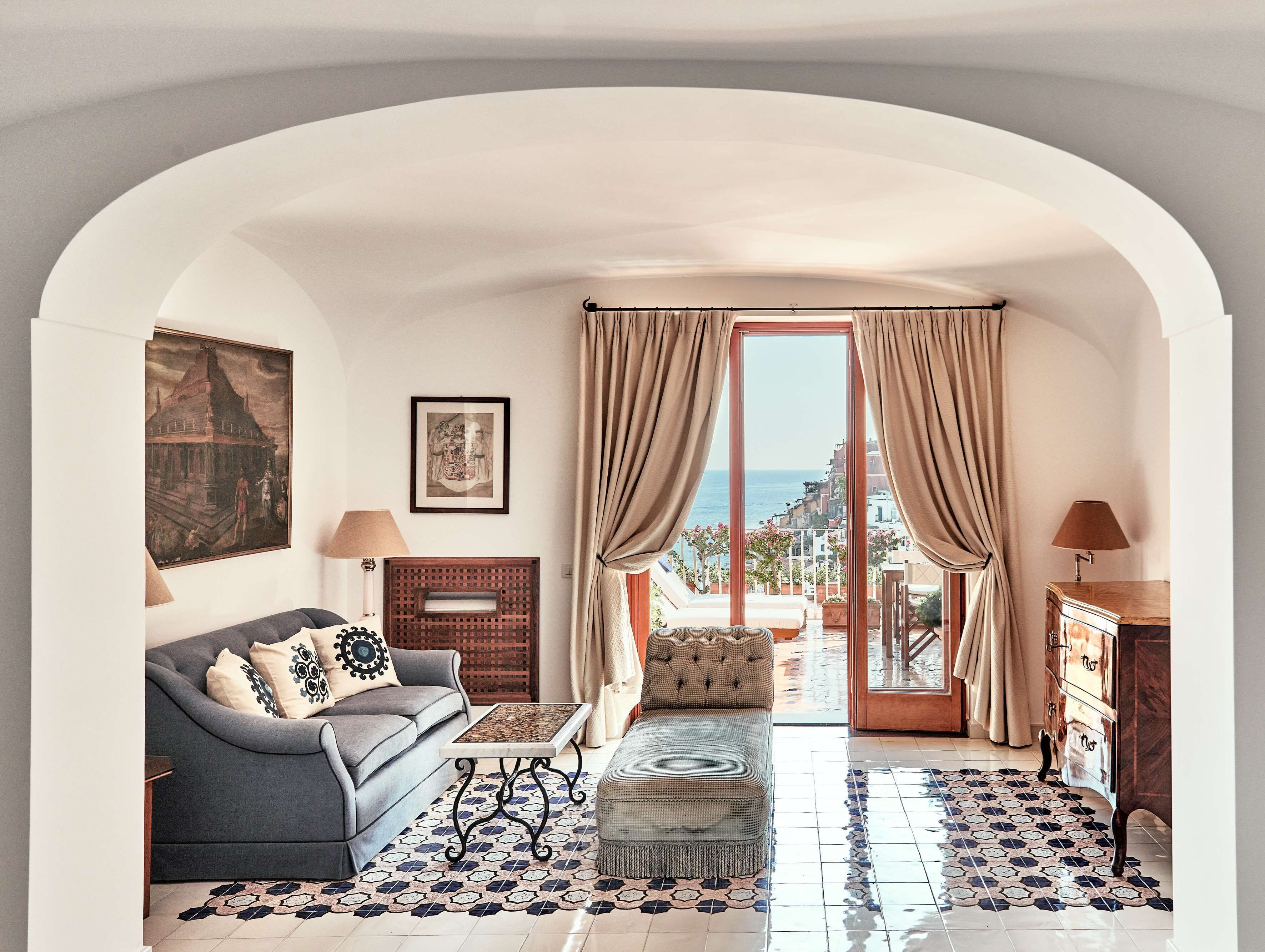 Una sala de estar acogedora con sofá, reposapiés y una mesita de centro. Cuenta con una chimenea, vistas al mar a través de un ventanal y un cuadro en la pared.