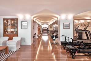 A spacious room with a wooden floor, a large bookshelf, exercise equipment, and a treadmill.