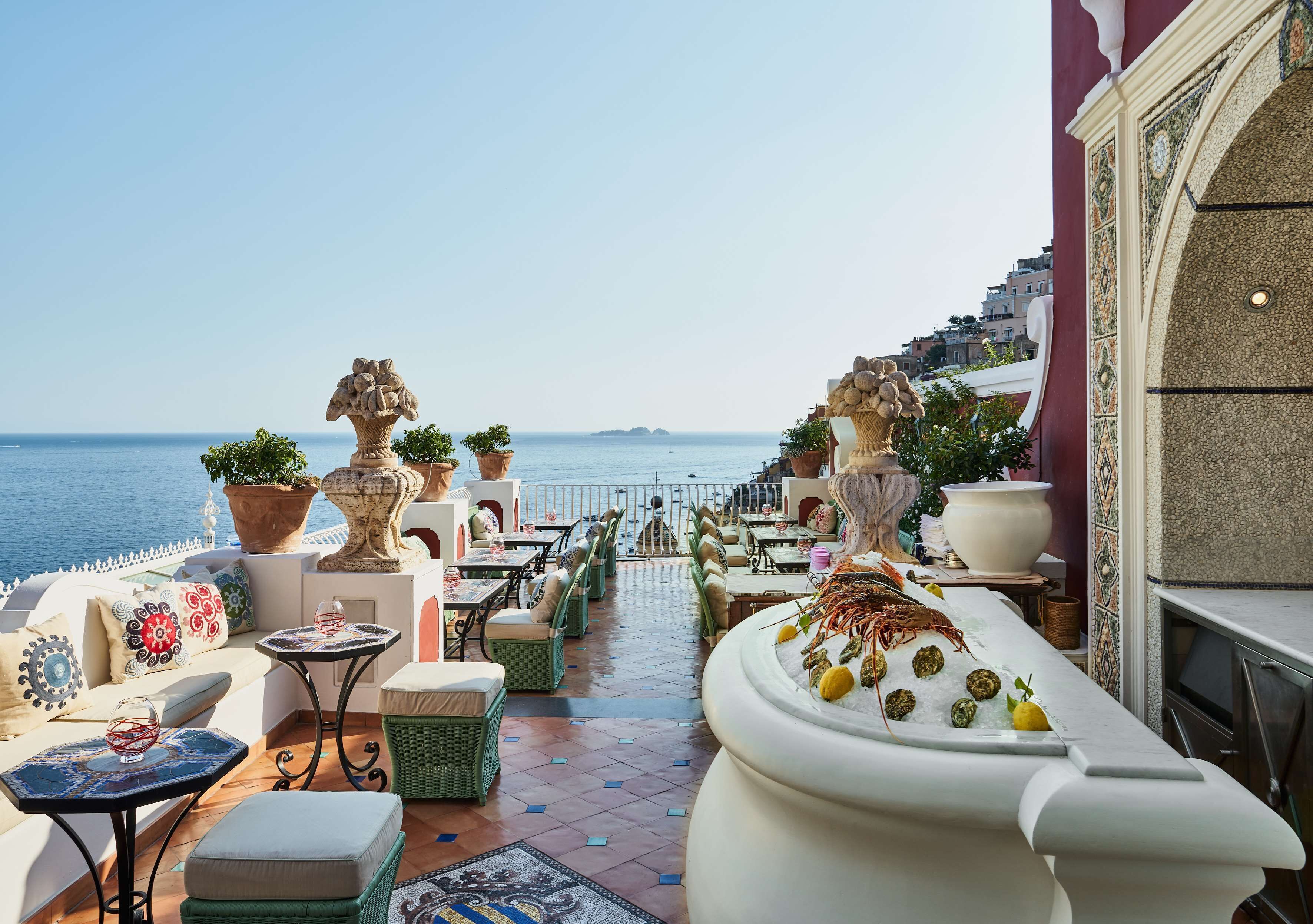 Une terrasse avec des sièges extérieurs, des plantes en pot et une vue sur la mer.