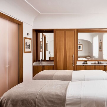 A hotel room with two beds, a wooden wardrobe, a vanity with a mirror, and framed pictures on the walls.