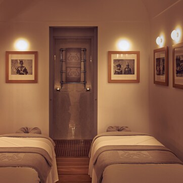 A hotel room with two beds, a wooden wardrobe, a shower area, and framed pictures on the wall.