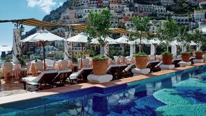 A poolside area with lounge chairs and umbrellas, overlooking a hillside of colorful buildings. - Le Sirenuse (Positano)