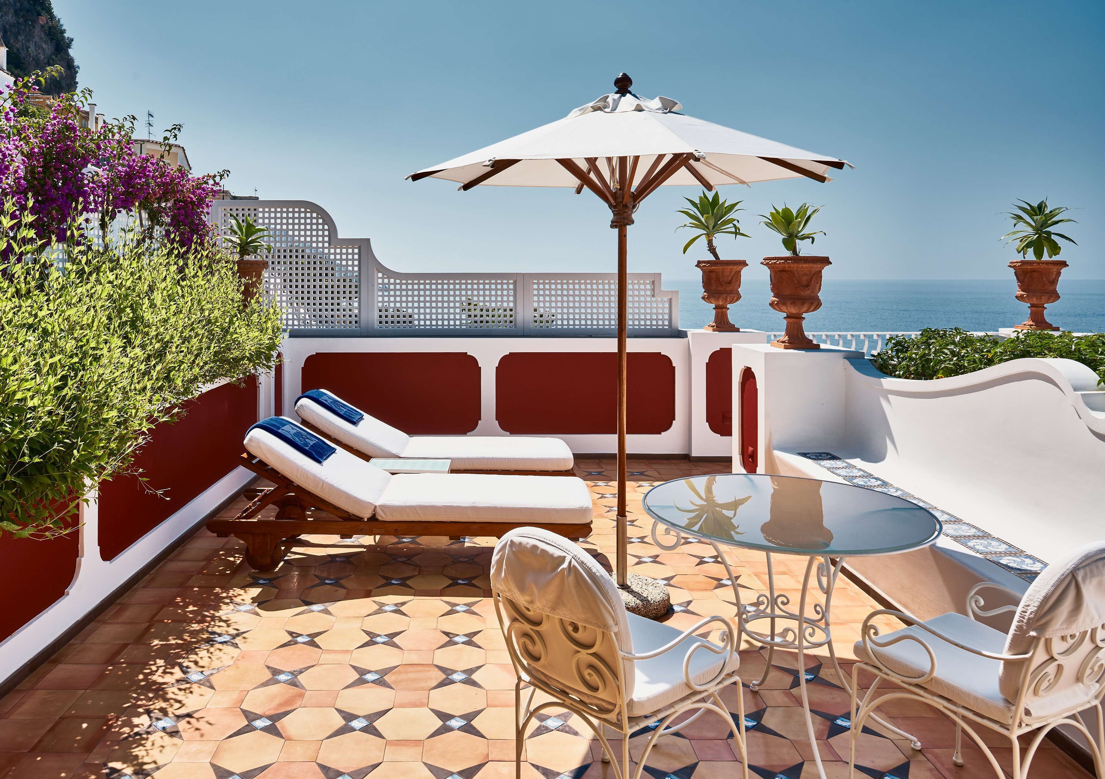A terrace with a white sofa, a dining table, and chairs, overlooking the sea.