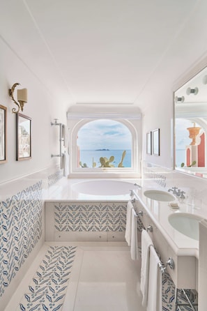 A bathroom with a large window, a bathtub, a sink, and a mirror.