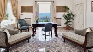 A room with a view of the sea, a table with chairs, and patterned floor tiles.