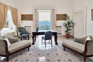 A room with a view of the sea, a table with chairs, and patterned floor tiles.