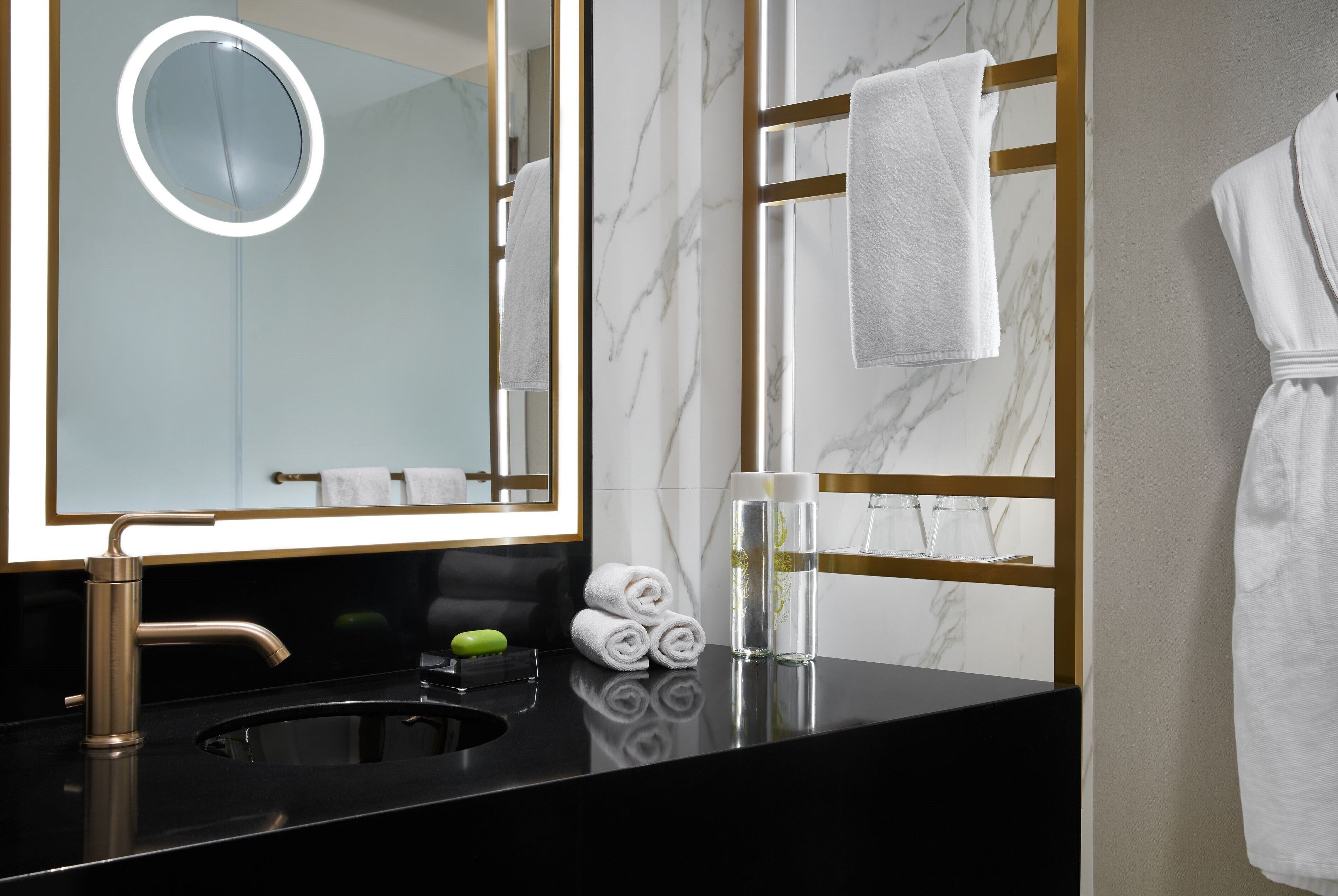 A modern bathroom with a black sink, a gold-framed mirror, and a marble wall.