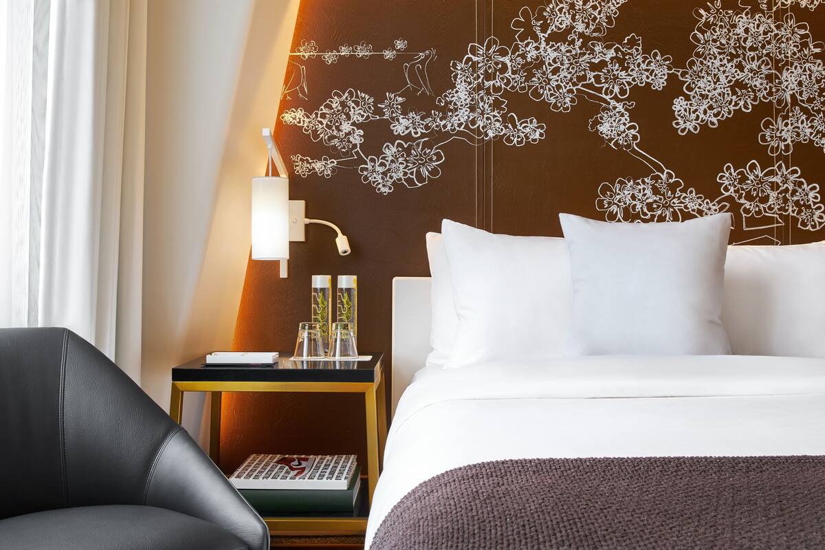 A hotel room with a bed, a nightstand, a lamp, and a chair.