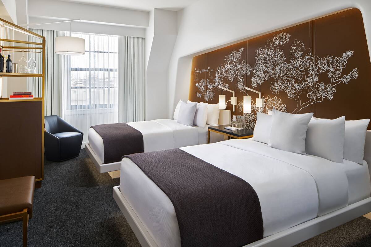 A hotel room with two beds, a desk, a chair, and a large window.