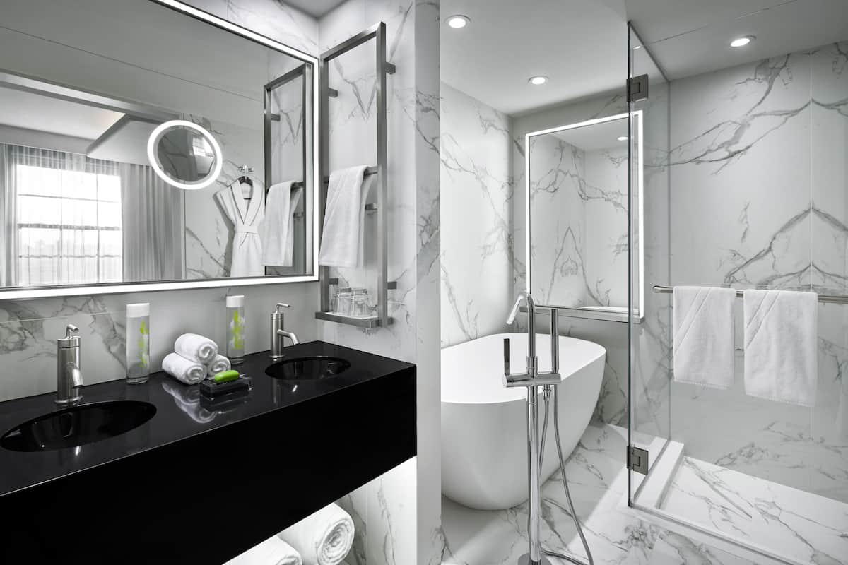 A modern bathroom with two sinks, a large mirror, and a walk-in shower.