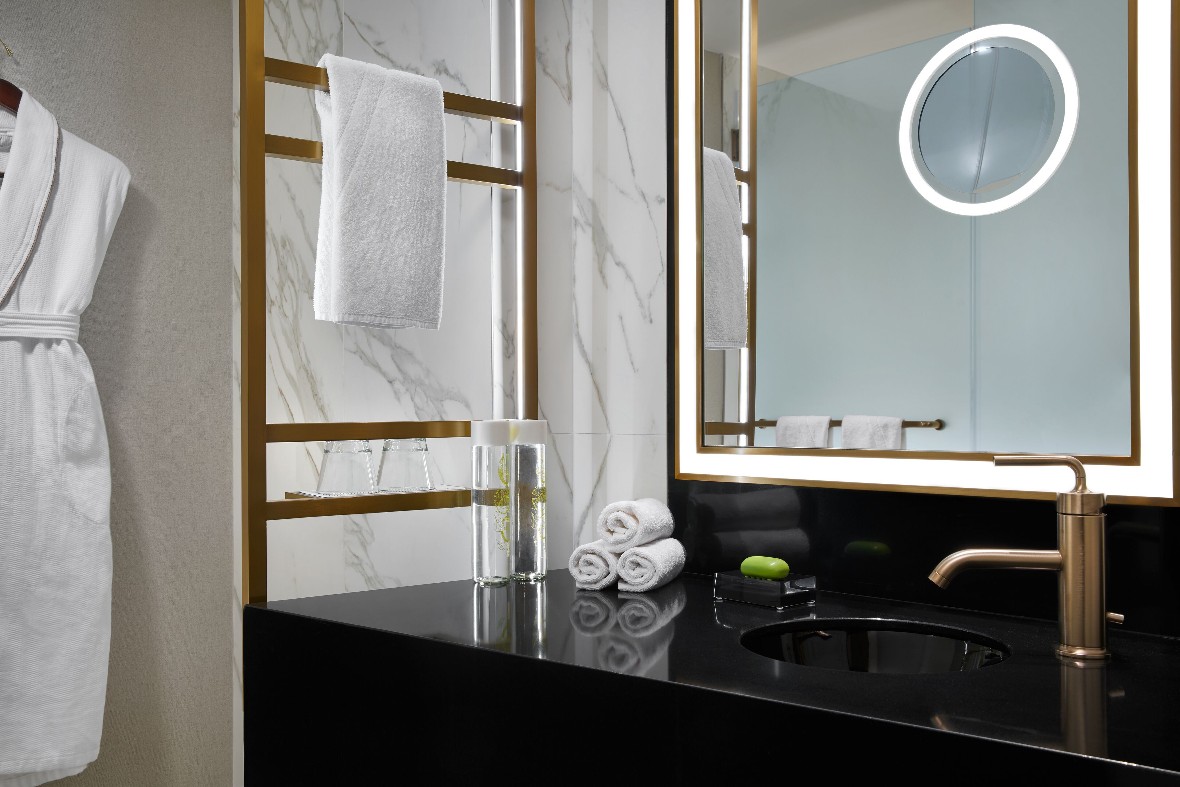 Une salle de bain moderne avec un mur en marbre, un lavabo noir, un miroir encadré d’or et un porte-serviettes avec des serviettes pliées.