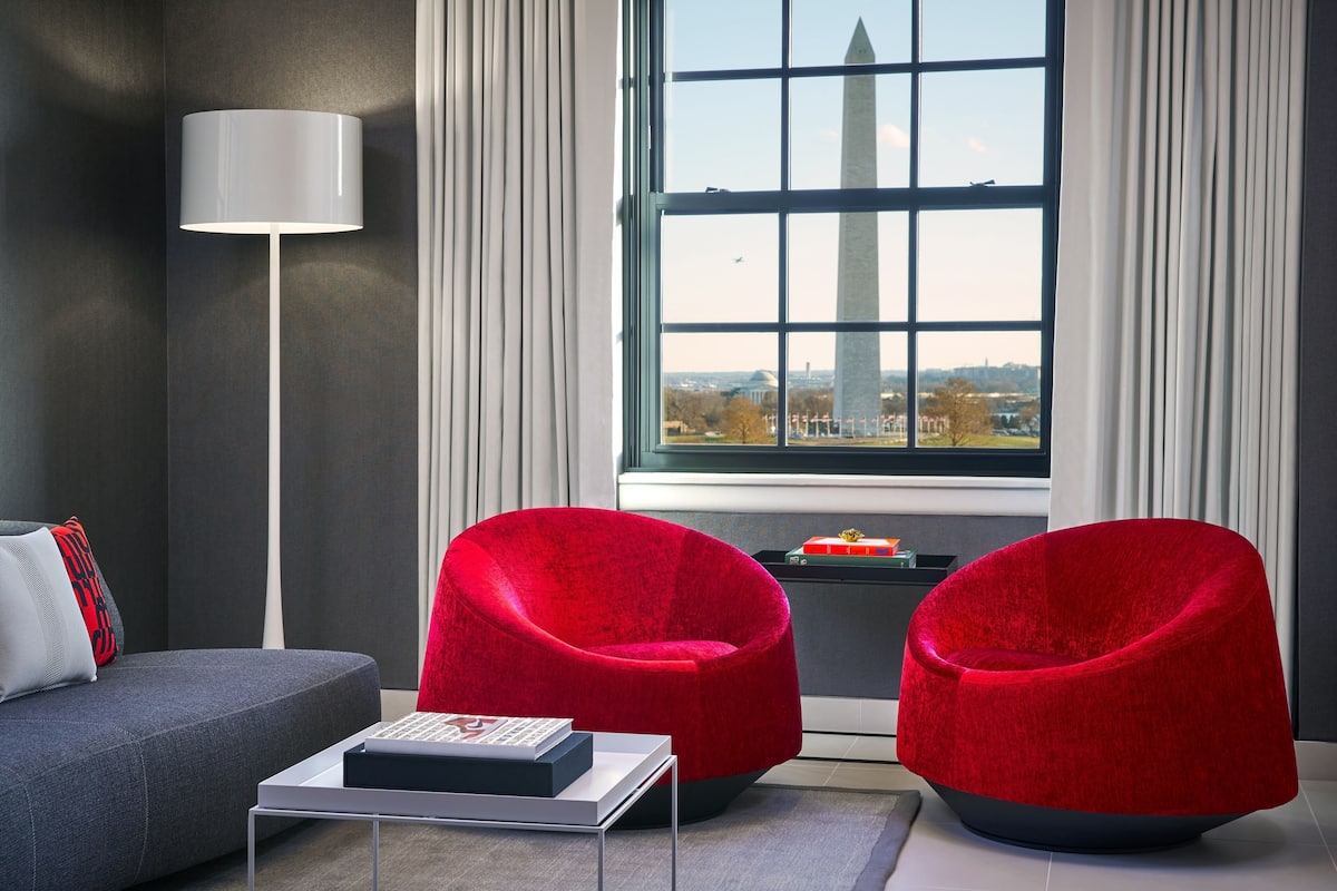 A modern living room with a view of the Washington Monument, a grey sofa, a red armchair, and a white coffee table.