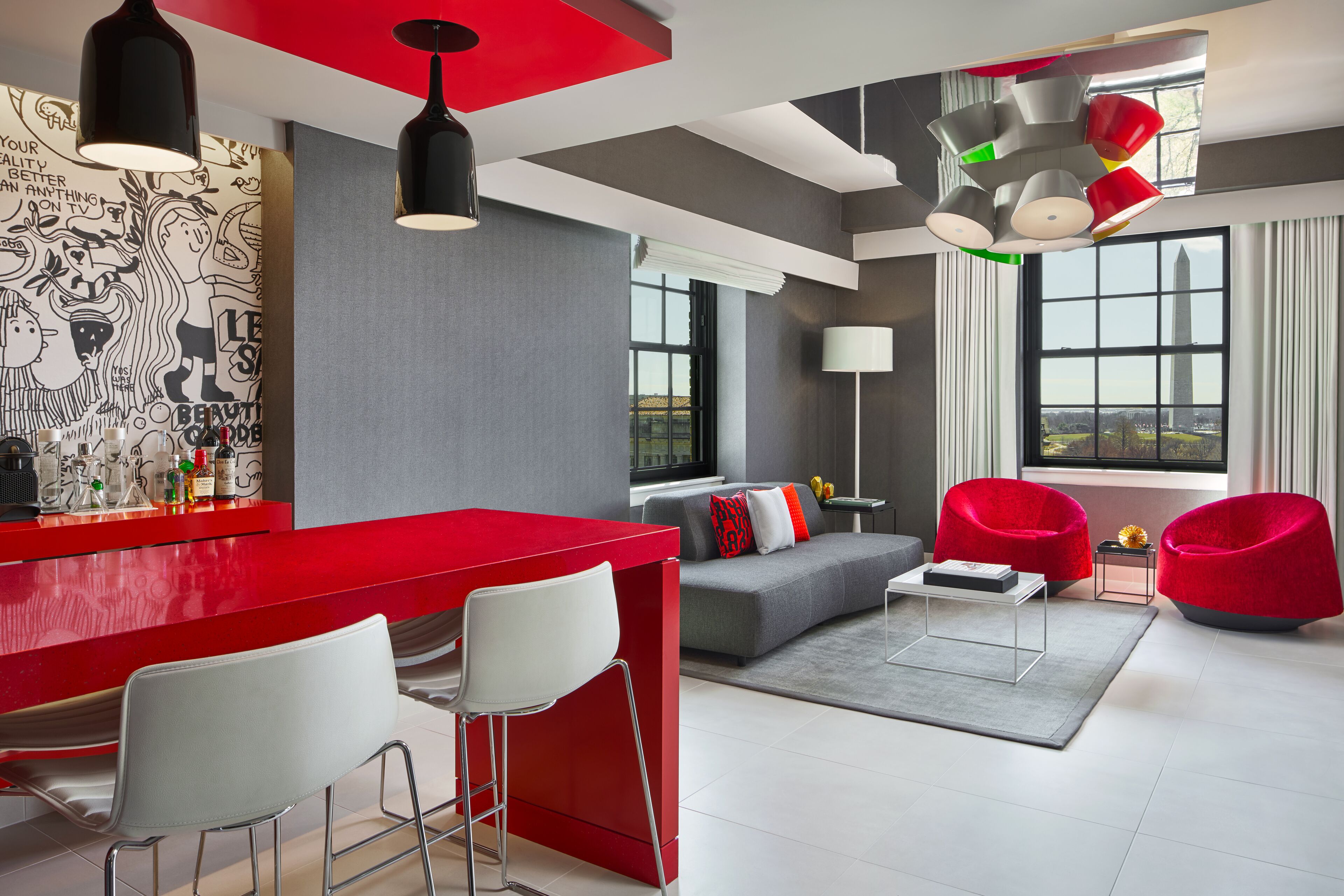 Een moderne woonkamer met een rode bar, een grijze bank en rode fauteuils.