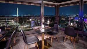 A rooftop dining area with tables and chairs, a city view, and the Washington Monument in the background.