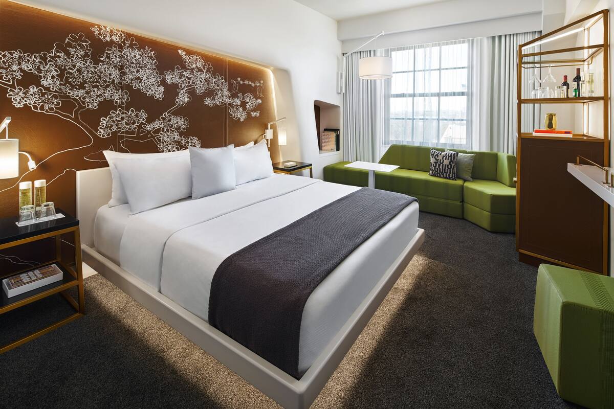 A modern hotel room with a large bed, a green sofa, a small table, and a wardrobe.