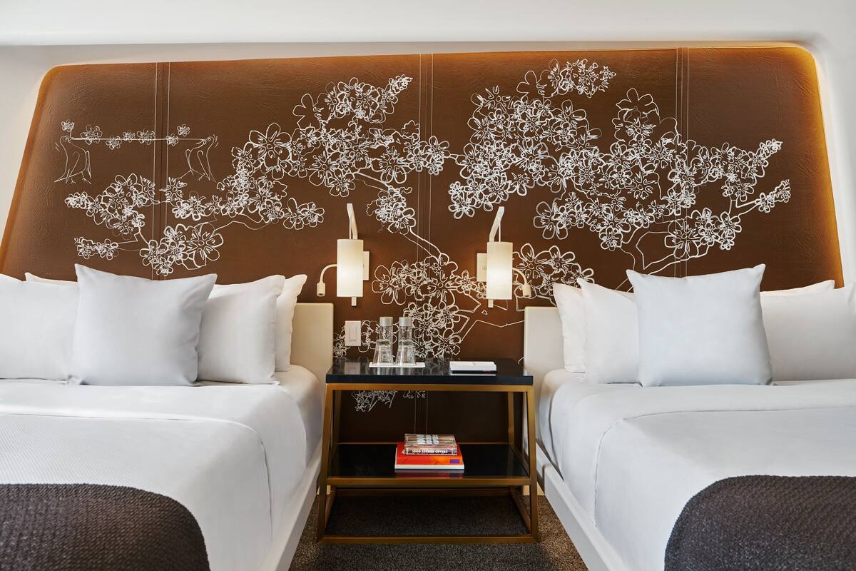 A hotel room with two beds, a nightstand with a lamp, and a decorative wall with floral patterns.