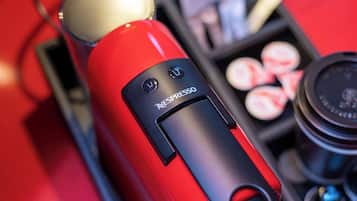 Punainen Nespresso-kahvinkeitin, jossa on vesisäiliö ja kahvikapselit.