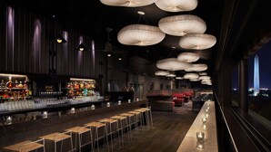 Un espace bar doté de plusieurs tabourets, d’un comptoir où sont exposées des bouteilles et de luminaires suspendus.