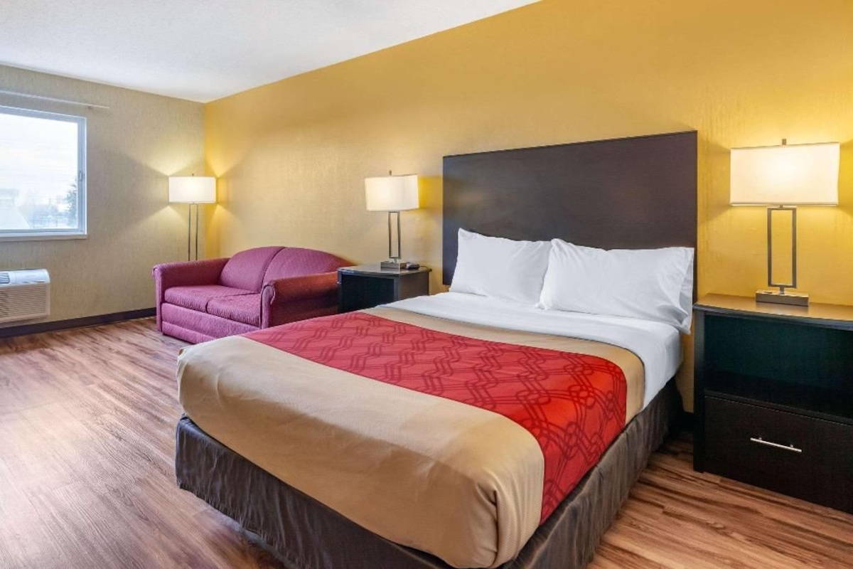 A hotel room with a large bed, two bedside tables with lamps, a chair, and a window.