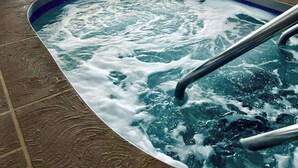 An indoor swimming pool with a hot tub, surrounded by lounge chairs and umbrellas, and a dining area with tables and chairs. -  Econo Lodge Wausau - Rothschild (Rothschild)