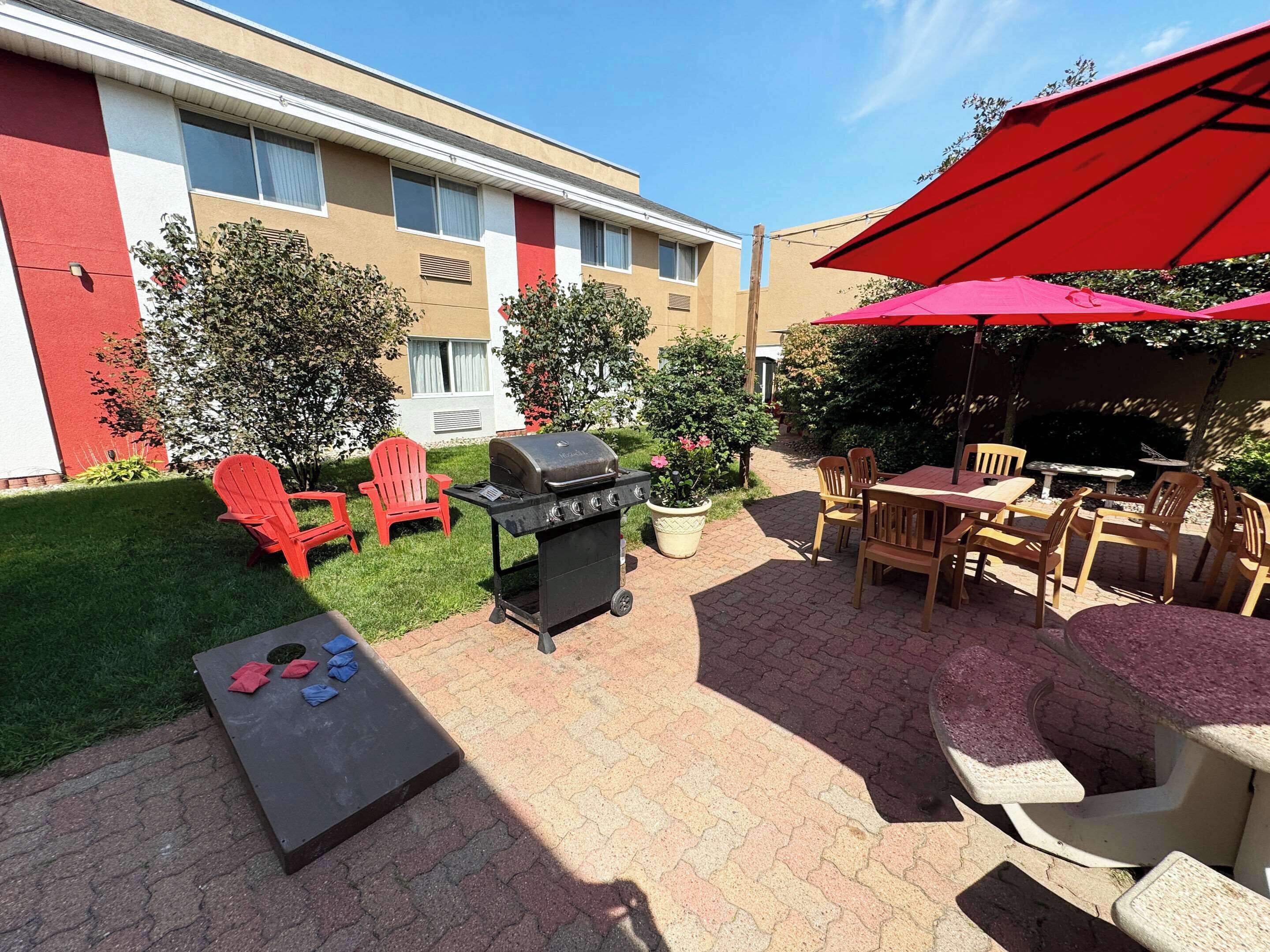 An outdoor patio with a grill, red chairs, and a table under a red umbrella.