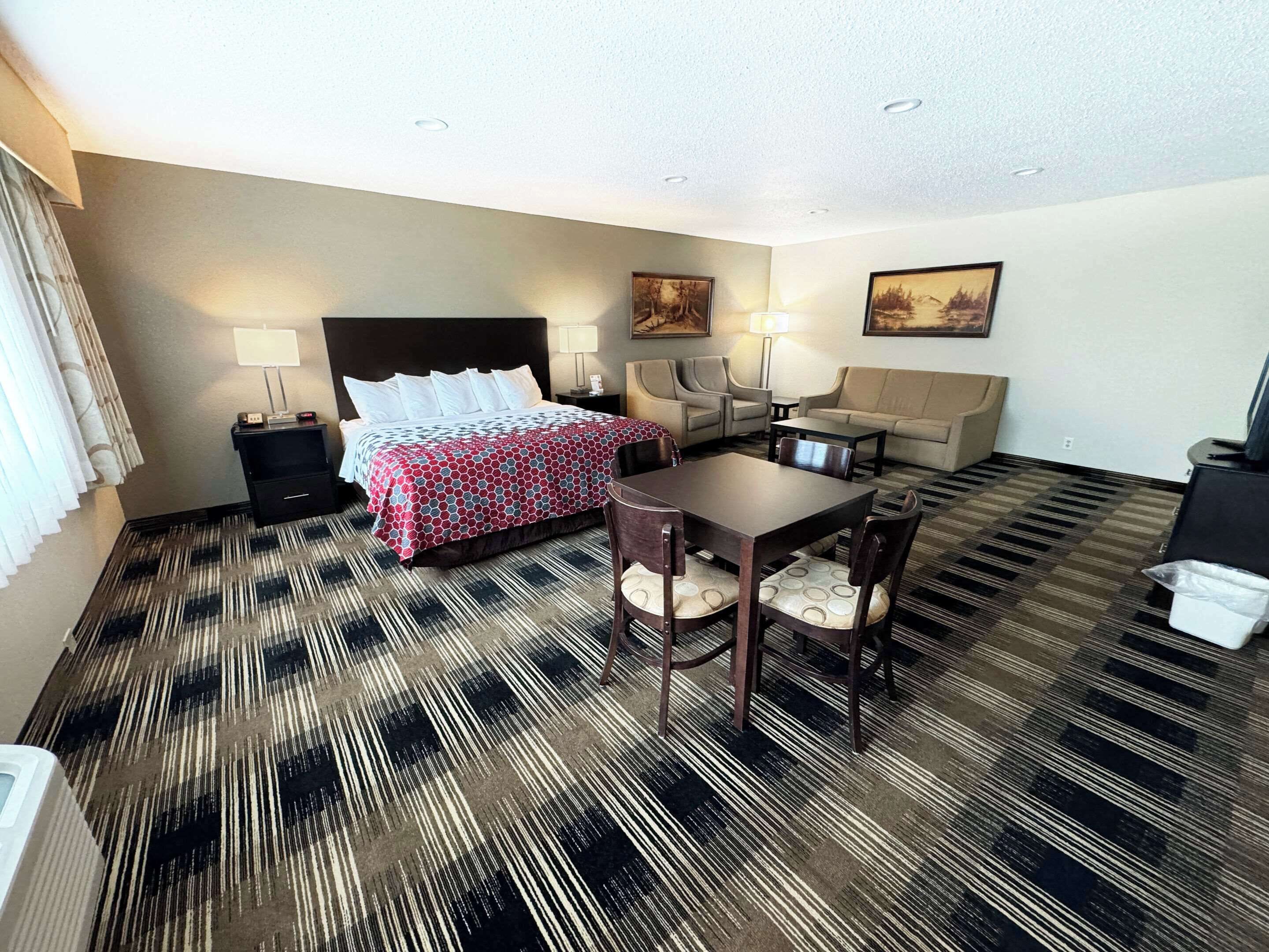 A hotel room with a bed, two chairs, a table, a sofa, and a desk.