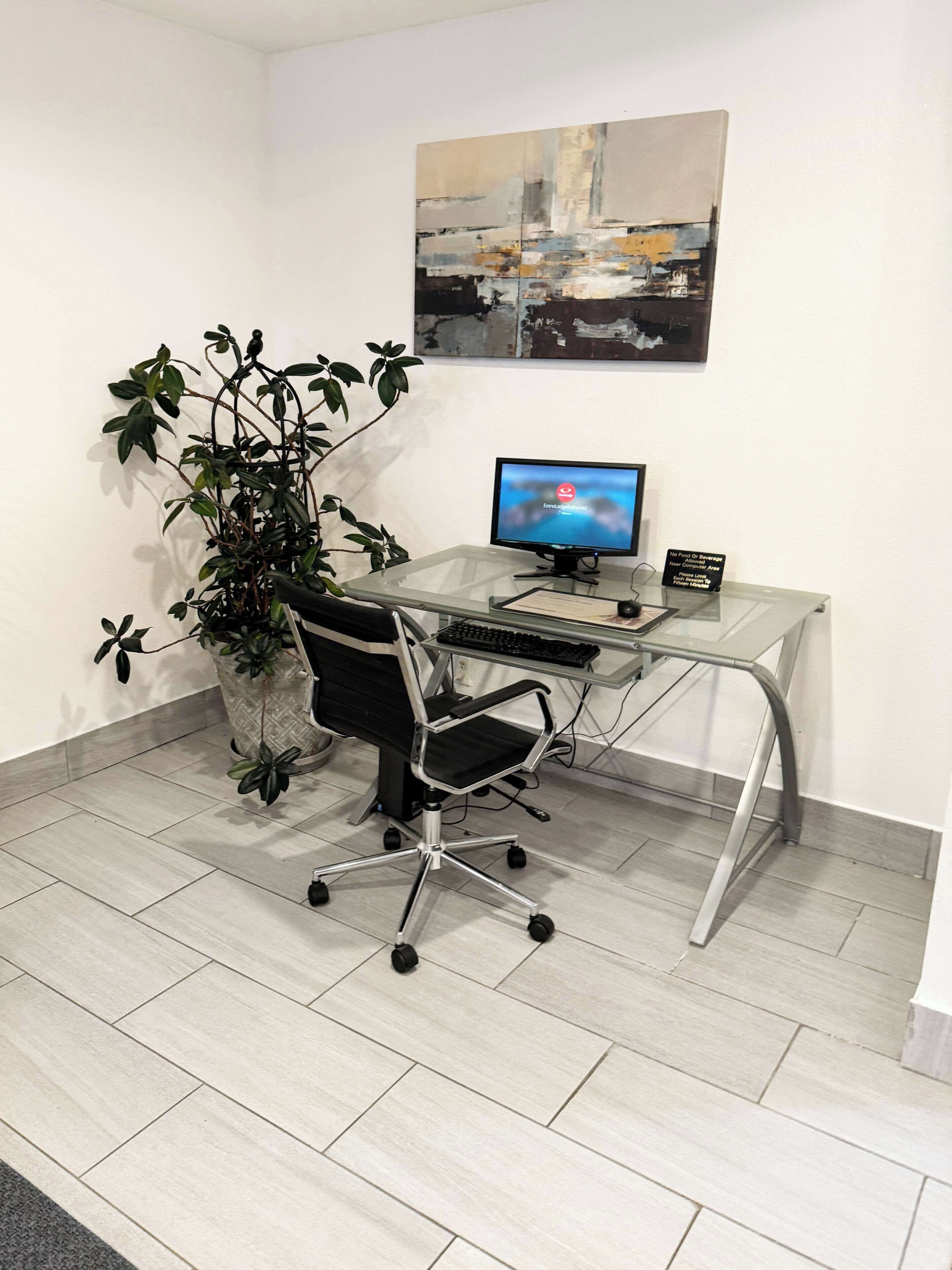 A modern office space with a glass desk, a black office chair, a computer monitor, and a potted plant.