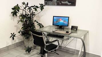 A modern office space with a glass desk, a black office chair, a computer monitor, and a potted plant.