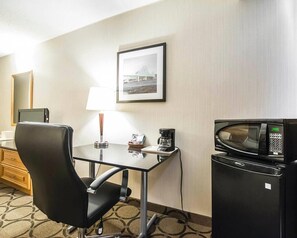 A hotel room with a desk, chair, lamp, coffee maker, microwave, and a framed picture on the wall. - Clarion Pointe (Campbellton)