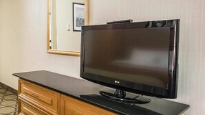 Une chambre d’hôtel avec un téléviseur à écran plat posé sur une commode en bois, un miroir au mur et une moquette à motifs.