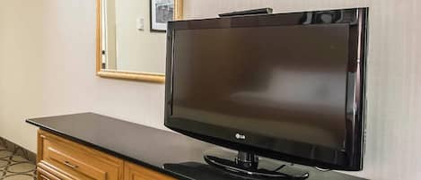 Habitación de hotel con televisor de pantalla plana sobre una cómoda de madera, un espejo en la pared y una alfombra estampada.