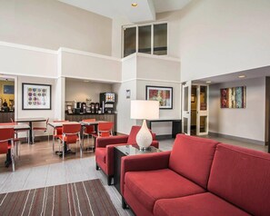 A hotel lobby with a dining area, red seating, a coffee machine, and artwork on the walls. - Clarion Pointe (Campbellton)