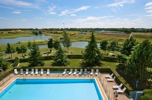 A swimming pool with sun loungers and a view of a golf course and water bodies. - Novotel Saint-Quentin en Yvelines (Magny-les-Hameaux)