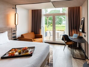 A hotel room with a bed, a desk with a laptop, a chair, a tray with breakfast, and a view of the outdoors. - Novotel Saint-Quentin en Yvelines (Magny-les-Hameaux)