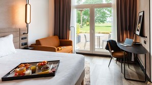 Habitación de hotel con una cama, un escritorio con una computadora portátil, una silla, una bandeja con desayuno y vistas al exterior.