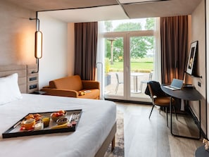 A hotel room with a bed, a desk with a laptop, a chair, a tray with breakfast, and a view of the outdoors.