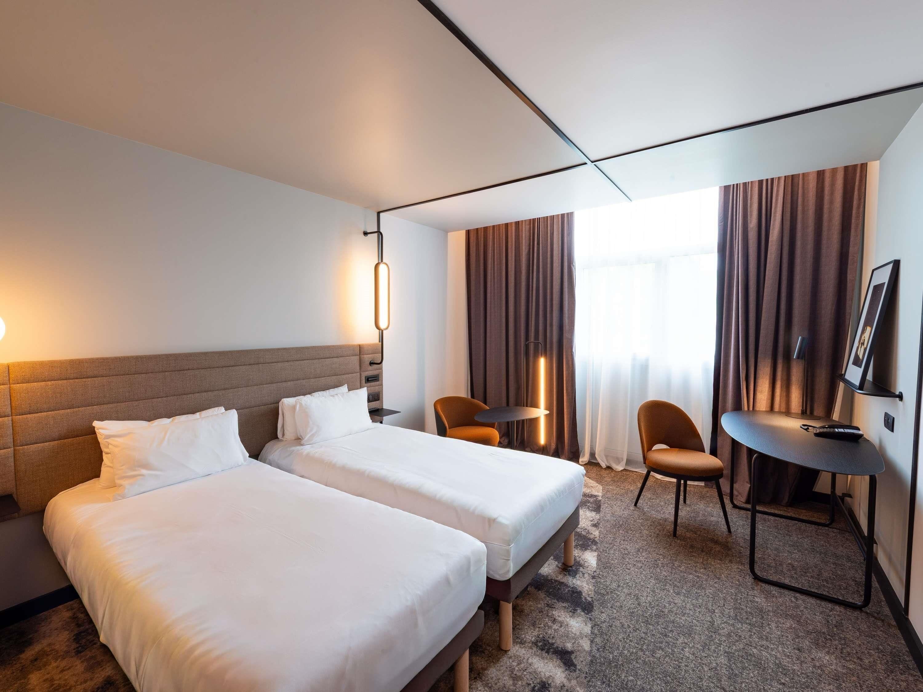 Ein Hotelzimmer mit zwei Betten, einem Schreibtisch, einem Stuhl, einem Fernseher und einem Fenster mit Vorhängen.