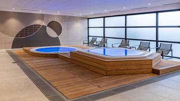Un espace piscine intérieur moderne, doté de deux bains à remous et de coins salon.