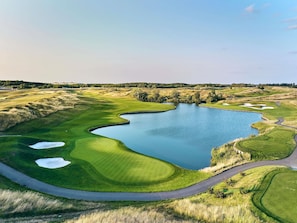 A golf course with a pond, sand bunkers, and a winding road.