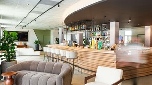 Un área de bar moderna con una barra curva, taburetes y un espacio de estar con un sofá y sillones.
