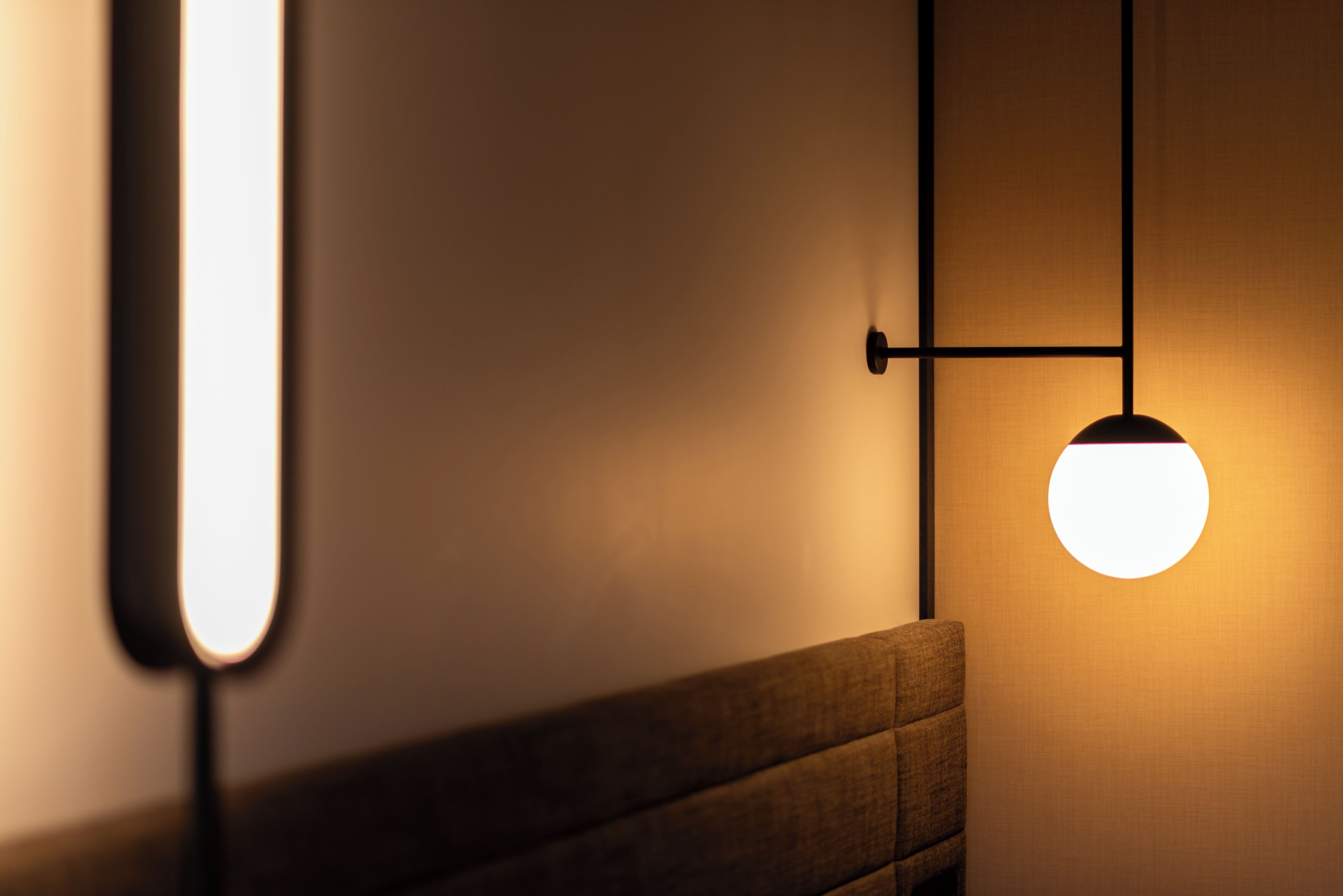 A wall-mounted light fixture with a round bulb, a horizontal light strip, and a wooden bench.