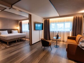 A modern hotel room with a bed, a sofa, a TV, and a small table. - Novotel Saint-Quentin en Yvelines (Magny-les-Hameaux)