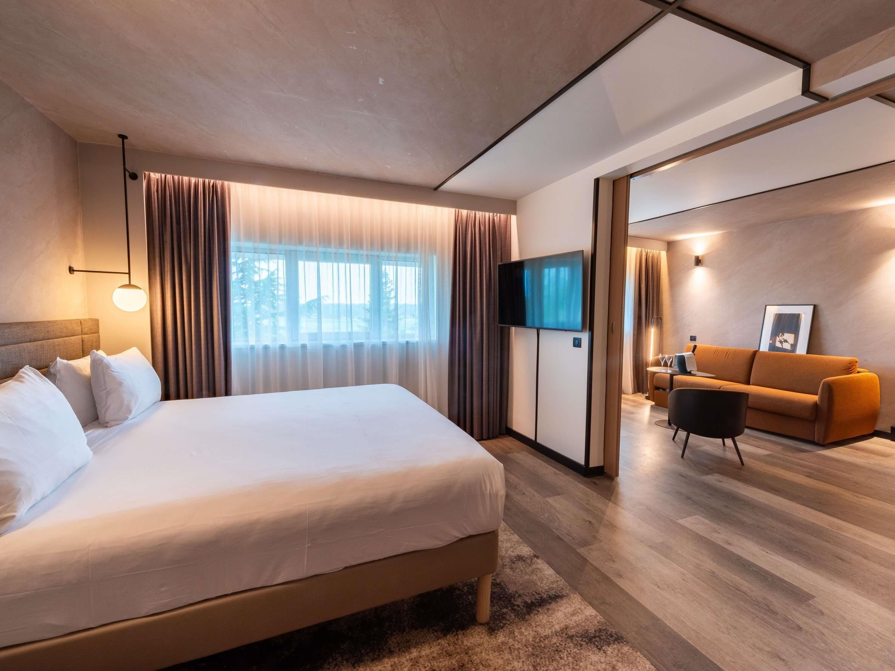 Una habitación de hotel moderna con una cama grande, un televisor de pantalla plana, un sofá y un rincón de comedor.